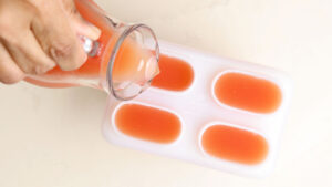 Pouring guava juice into popsicle molds.